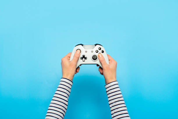 руки, держащие геймпад на синем фоне. знамя. концептуальные игры, видеоигры - game controller стоковые фото и изображения