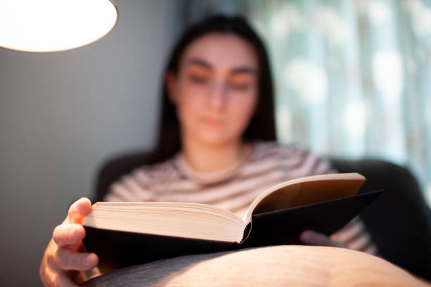istock Young woman reading a book under a reading lamp 1252389120