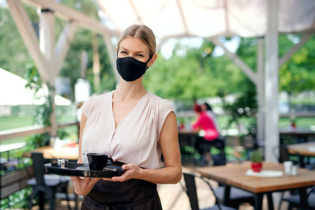 garçonete com máscara facial servindo clientes ao ar livre no restaurante terraço. - starbucks women walking restaurant - fotografias e filmes do acervo