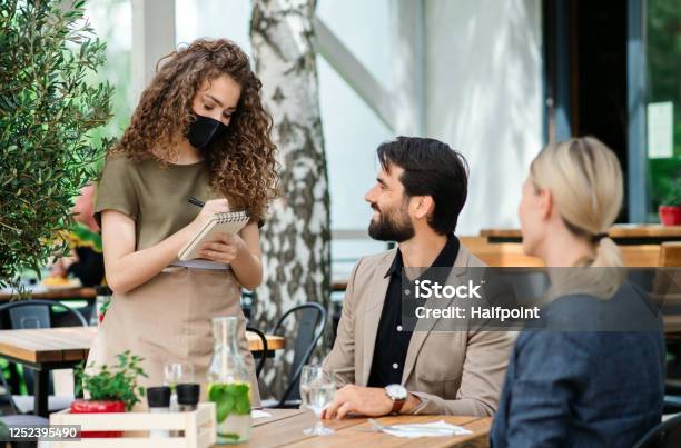 Waitress With Face Mask Serving Happy Couple Outdoors On Terrace Restaurant Stock Photo - Download Image Now