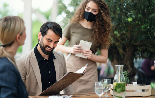 istock Waitress with face mask serving happy couple outdoors on terrace restaurant. 1252395535