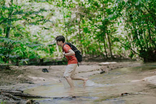 an asian chinese young man jungle trekking crossing river