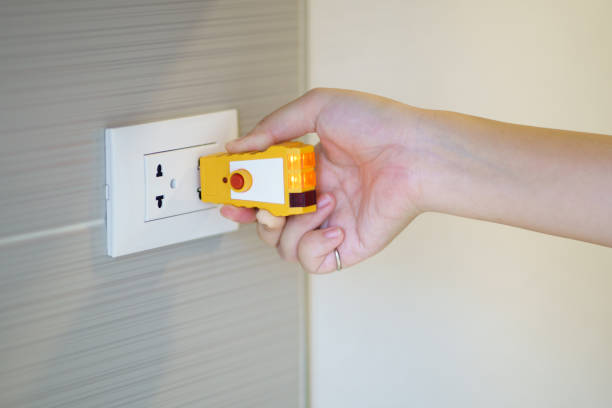 tester elettrico con mano per il controllo della spina alla presa di corrente sul muro. controlla la qualità dell'elettricità in casa. concetto di acquisto di una nuova casa ispezione e manutenzione della casa - electric plug outlet human hand electricity foto e immagini stock