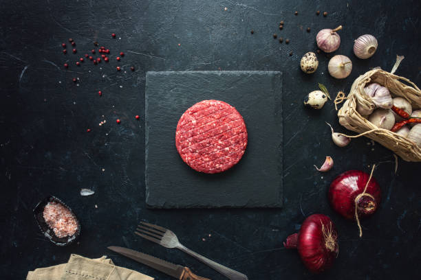 Raw minced beef burgers with spices layout Raw minced beef burgers with spices layout on aged wooden cutting board. Directly above shot ground beef photos stock pictures, royalty-free photos & images