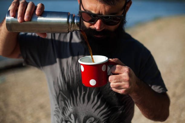 An attractive guy pours coffee into a pot on the beach stock photo