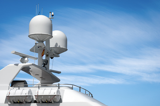 Upper part of a white luxury yacht with the navigational equipment on blue sky with clouds