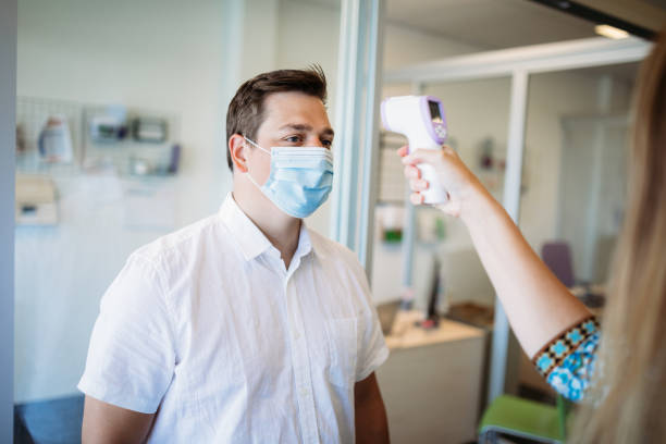 istock Man Has Temperature Taken By Office Worker Wearing Mask 1252415136