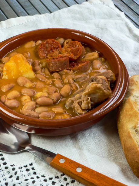 istock Asturian fabada, typical Spanish in a clay plate on wooden table with white tablecloth, top view 1252415369