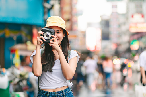 Travel vacation city concept, Young happy traveler asian woman with instant camera and backpack walking on Yaowarat Road outdoor market in Bangkok, Thailand