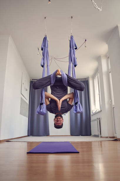 homme d’athlétisme faisant la pose de pigeon inversé tout en pratiquant le yoga aérien - inversion yoga photos et images de collection