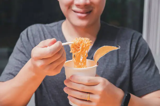A man holding a plastic fork with cooked instant noodles. Instant noodle is convenient and delicious food.