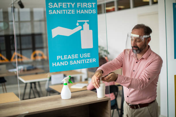 istock Teacher with face shield disinfecting hands with hand sanitizer before entering classroom 1252421393