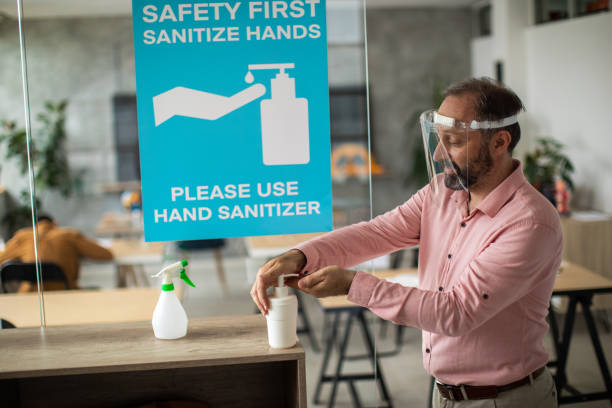 istock Teacher with face shield disinfecting hands with hand sanitizer before entering classroom 1252421461