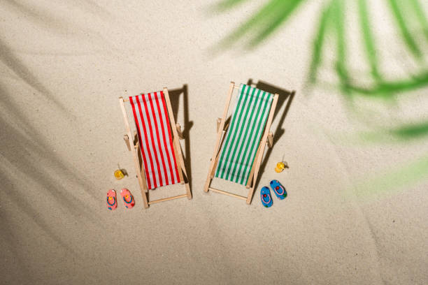 vue aérienne deux chaise de pont, verre de jus, tongs sur le sable à travers les branches du palmier et du palmier d’ombre. voyage, vacances, été, concept romantique. vue supérieure. - beach tropical climate palm tree deck chair photos et images de collection