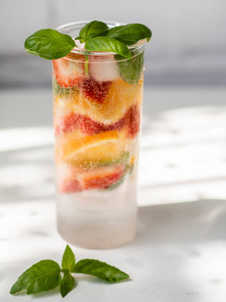 Fresh Summer Homemade lemonade with orange slices, strawbereies, basil and ice in glass on a white table. stock photo