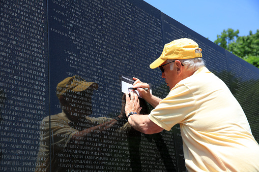 Washington DC, USA - May 02, 2019: Volunteer take a rubbing of a Name at the Vietnam War Memorial on the Mall in Washington DC. The Names are in chronological order,from first casualty in 1959 to last in 1975. USA