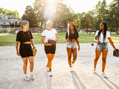 Diverse group of young women going for practice of soft ball at the outdoor city park field.
