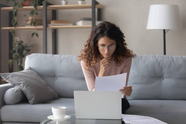 istock Thoughtful woman wearing glasses reading document, using laptop 1252459162