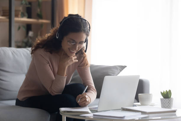 istock Smiling woman wearing headphones writing notes, studying online 1252459185