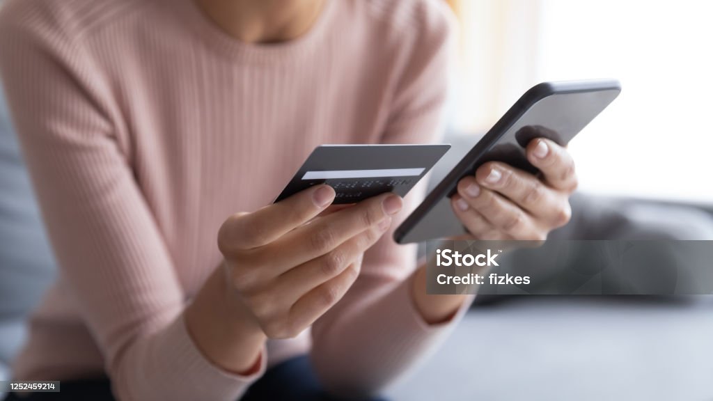 Close up female hands holding credit card and smartphone Close up female hands holding credit card and smartphone, young woman paying online, using banking service, entering information, shopping, ordering in internet store, doing secure payment Credit Card Stock Photo