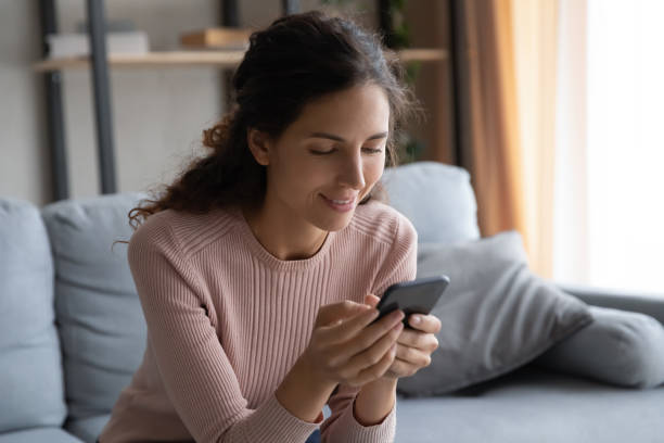 istock Smiling young woman using smartphone, sitting on cozy couch 1252459225