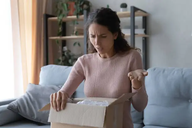 Photo of Angry confused woman unpacking parcel, wrong or broken order