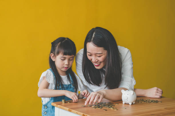 Young Asian Mother and her daughter count coins from piggy bank Young Asian Mother and her daughter count coins from piggy bank. counting coins stock pictures, royalty-free photos & images