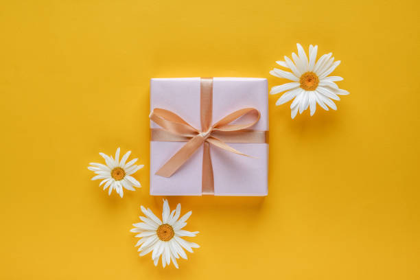istock Gift box with white daisy flowers on yellow background. Top view with copy space 1252463856