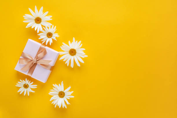 istock Gift box with white daisy flowers on yellow background. Top view with copy space 1252464389