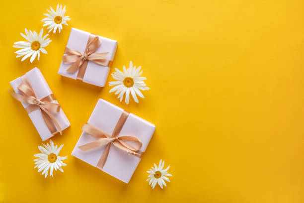 istock Gift box with white daisy flowers on yellow background. Top view with copy space 1252465451