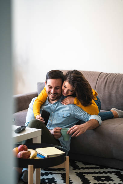 istock Smiling young couple embracing while looking at smartphone stock photo 1252471439