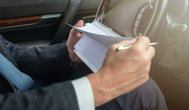istock Side view of a businessman hand taking notes in a planner while sitting in a car in suit. businessman planning in a car. Man looking his time planner 1252480753