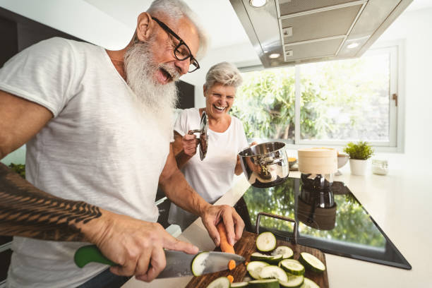 glückliches senior-paar mit spaß beim gemeinsamen kochen zu hause - ältere menschen bereiten gesundheit mittagessen in der modernen küche - ruhestand lifestyle familie zeit und lebensmittel-ernährung konzept - gourmet küche stock-fotos und bilder
