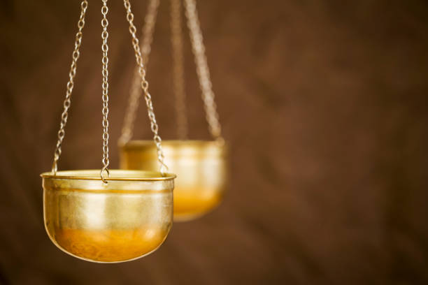 A justice scale on a desk next to a row of law books. Light filters in through a window in the background creating ample negative space for coy.  Photographed using a very shallow depth of field.