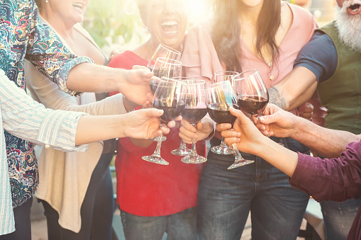 Happy family toasting with red wine glasses at dinner outdoor - People having fun cheering and drinking while dining together - Food and beverage weekend lifestyle activities