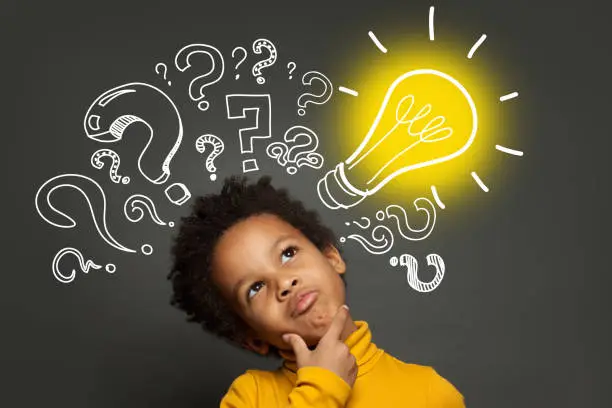 Photo of Thinking child boy on black background with light bulb and question marks. Brainstorming and idea concept