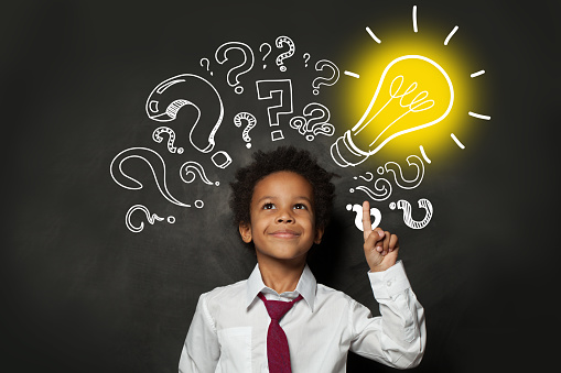 Smiling black child student with lightbulb on blackboard background. Brainstorming and idea concept