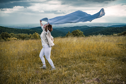 Adult woman is holding fabric on wind in nature