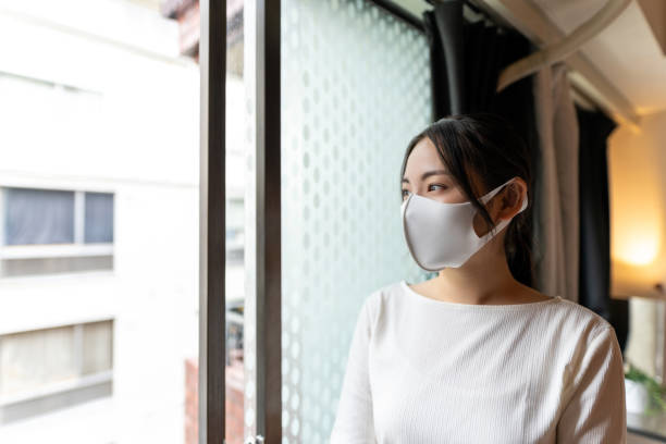 istock Asian woman with mask standing by the window 1252495251