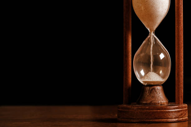 A wooden vintage hourglass sits on an isolated white background. Close up