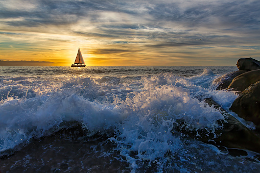 A Sailboat is Sailing Along the Ocean as a Wave is Breaking on the Shore