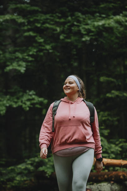 istock Spending the Day in Nature: a Plus Size Woman in a Pink Sweatshirt Wearing a Backpack While Hiking in the Forest 1252521200