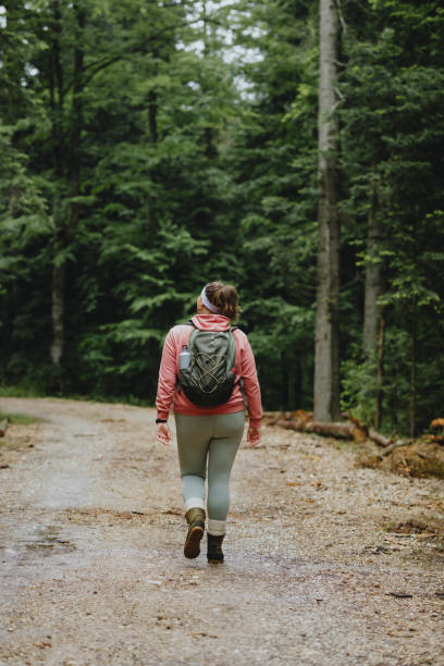 istock Spending the Day in Nature: a Plus Size Woman in a Pink Sweatshirt Wearing a Backpack While Hiking in the Forest 1252521240