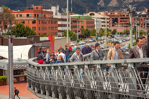 Bogota, Colombia - May 17, 2017: Local Colombian people seen climbing up a ramp that leads to a footbridge and on to a Bus Rapid Transit station on Calle 125 in the capital city. In the background is a Drive Through McDonald's outlet, office and apartment buildings. A parking lot can also be seen. In the far background are the Eastern Hills of the city. The altitude at street level is about 8500 feet above mean sea level. Horizontal format.