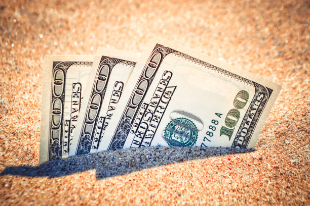istock Money dolars half covered with sand lie on beach close-up. 1252577962