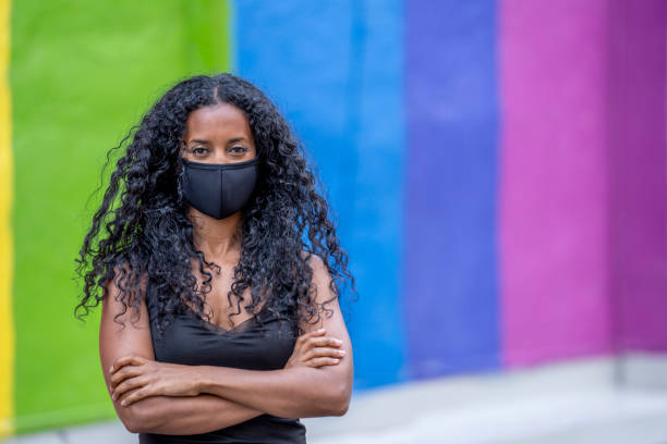 Beautiful African American Woman Wearing a Protective Face Mask Woman in her 20s wearing a protective face mask to protect herself from the transfer of germs during COVID-19 outbreak, standing in front of a pride mural. anti racism photos stock pictures, royalty-free photos & images