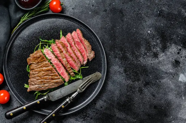 Grilled and cut Flat Iron steak. Marble beef meat. Black background. Top view. Copy space.