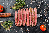 Grilled and sliced Flank rare steak. Marble beef meat. Black background. Top view
