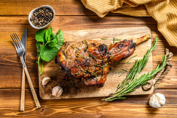 Roasted lamb, sheep leg on a cutting board with rosemary. wooden background. Top view Roasted lamb, sheep leg on a cutting board with rosemary. wooden background. Top view. celebrity roast stock pictures, royalty-free photos & images