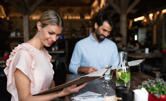 Happy young couple sitting indoors in restaurant, looking at menu.